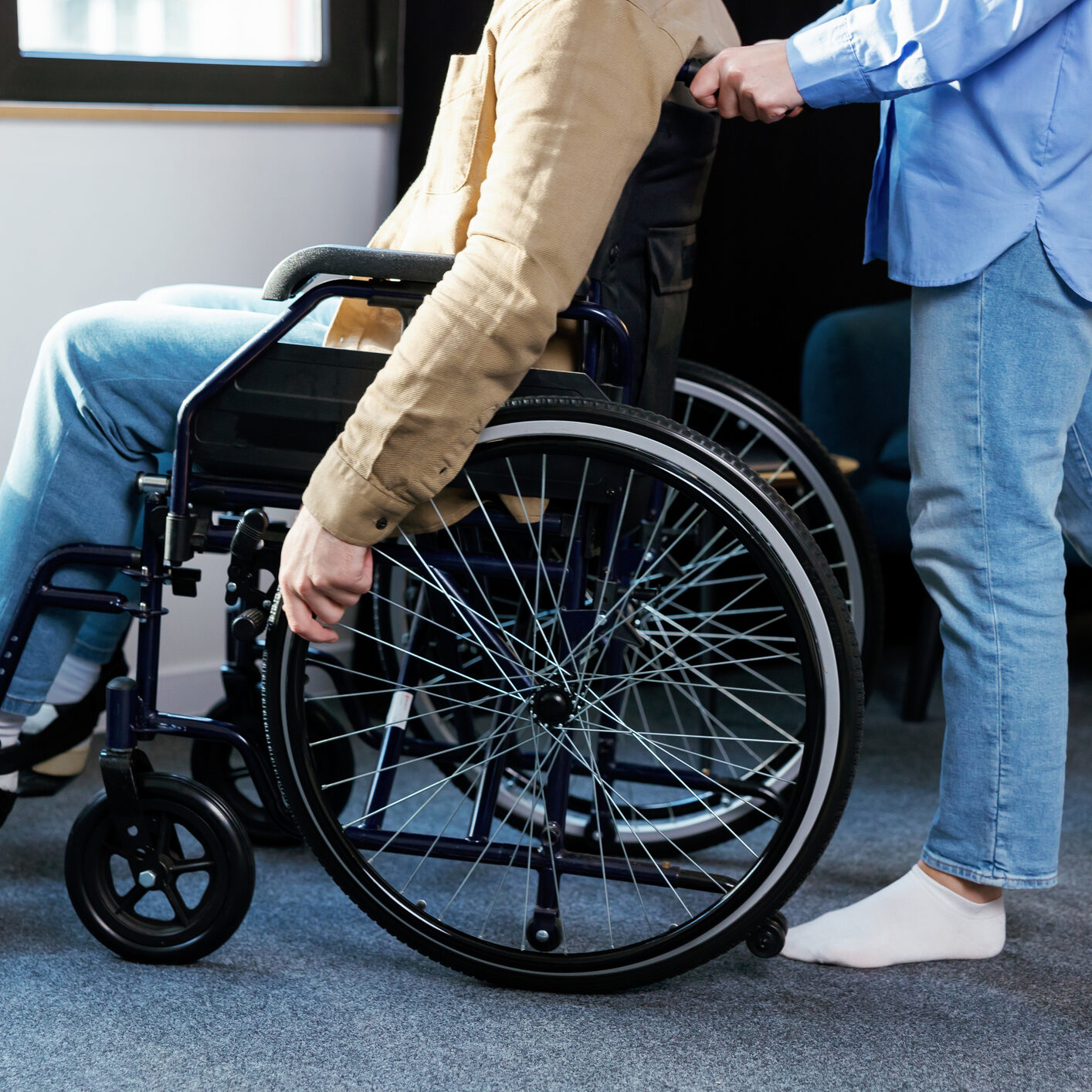A young pretty girl helps her friend who is confined to a wheelchair.